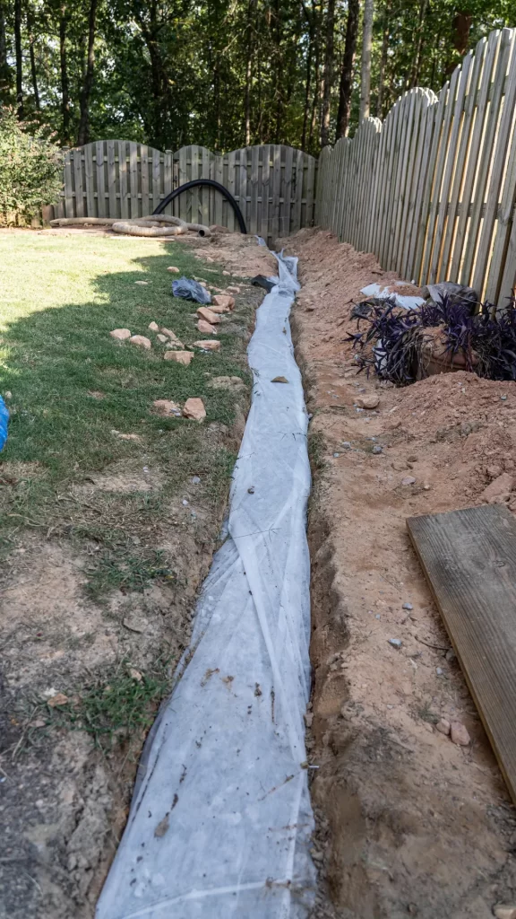 French Drain installation. Fabric covers drainage rock and pipe to keep a French drain clear of debris in this DIY home improvement project to alleviate drainage issues.